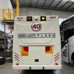 Photo of the rear of a 2024 Isuzu iBus bus with New South Wales TS150 Safebus SB001A surface mount school bus lights and signage