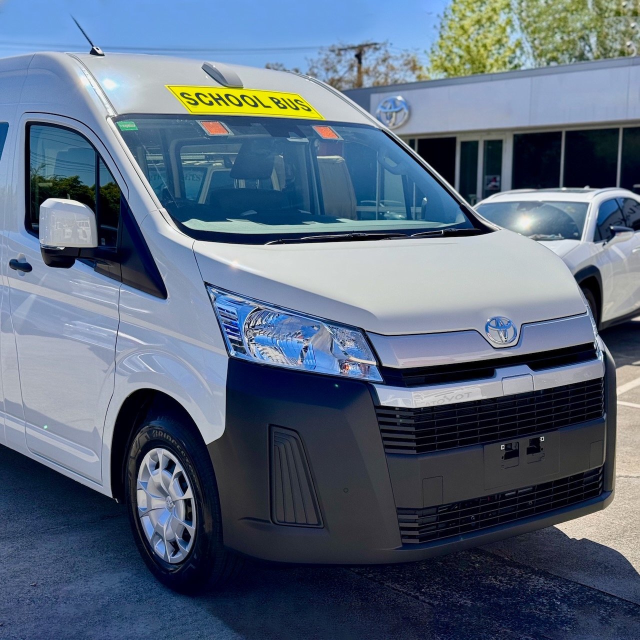 Two thirds photo of the front of a 2023 6th generation Toyota HiAce Commuter bus with Safebus interior mount Victorian school bus lights and signage installed