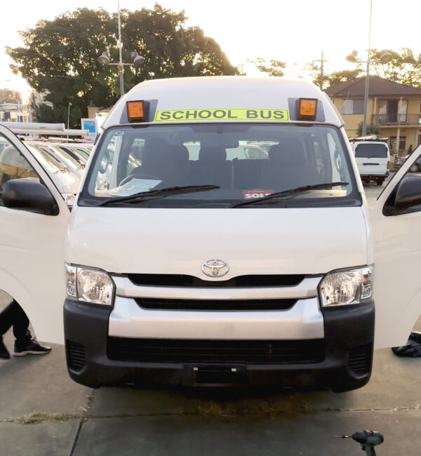 Photo of the front of a 2013 5th generation Toyota HiAce Commuter bus with Safebus NSW TS150 roof mounted school bus lights and signage installed