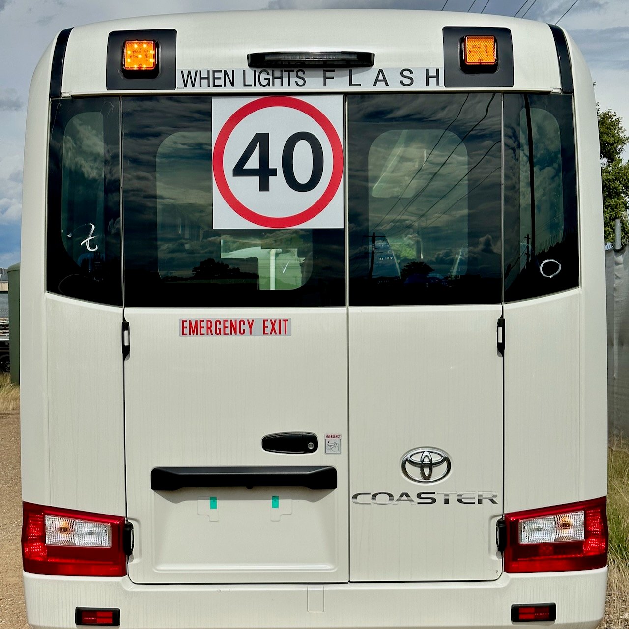 Photo of the rear of a 2024 4th generation B80 Toyota Coaster bus with Safebus SB001A surface mount New South Wales TS150 school bus lights and and Small When Lights Flash signage installed