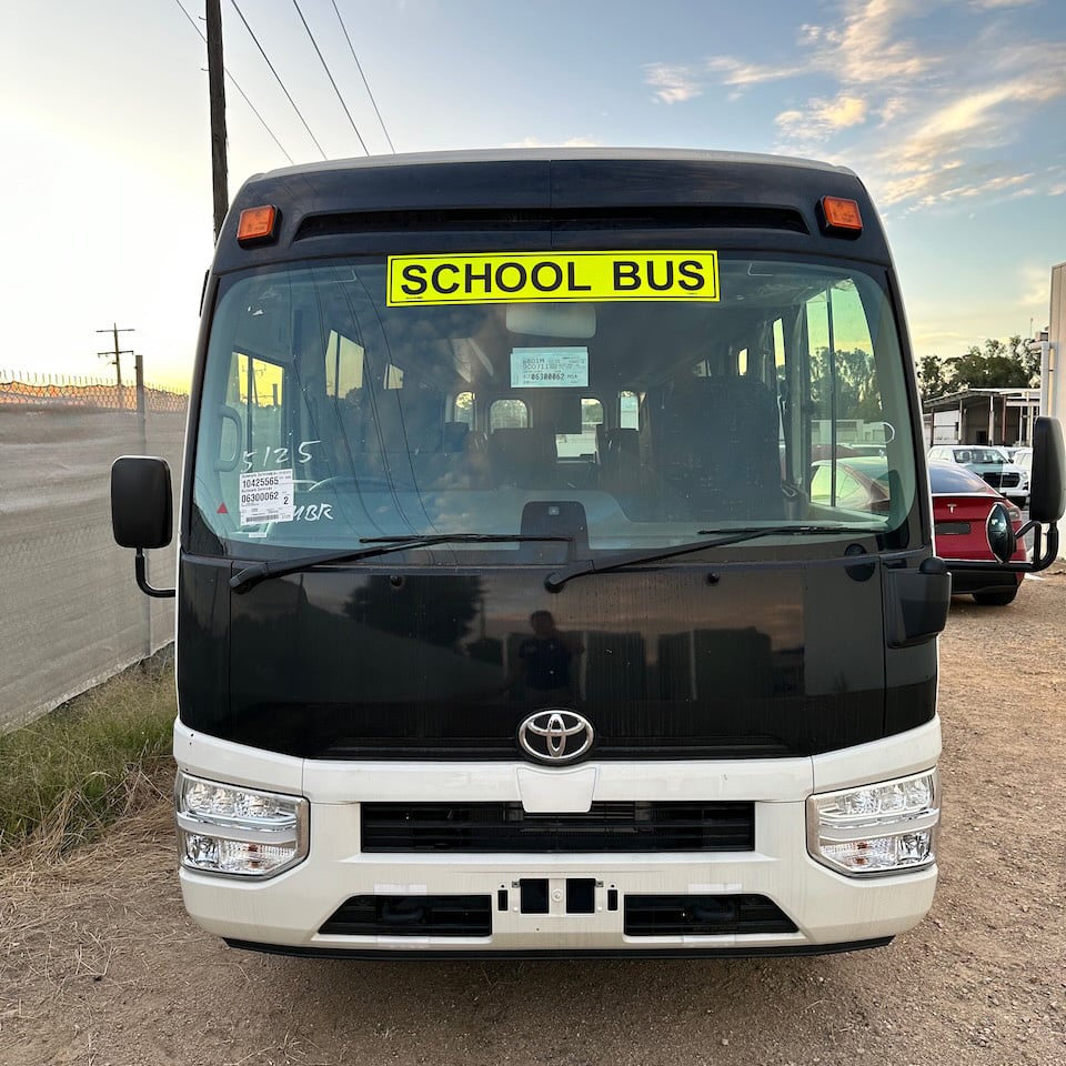 Photo of the front of a 2024 4th generation B80 Toyota Coaster bus with Safebus SB001A surface mount New South Wales TS150 school bus lights and signage installed