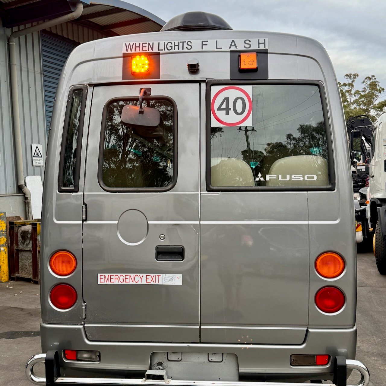 Photo of the rear of a Mitsubishi Rosa bus with NSW TS150 school bus lights and small 40km/h signage and chrome loop towbar installed