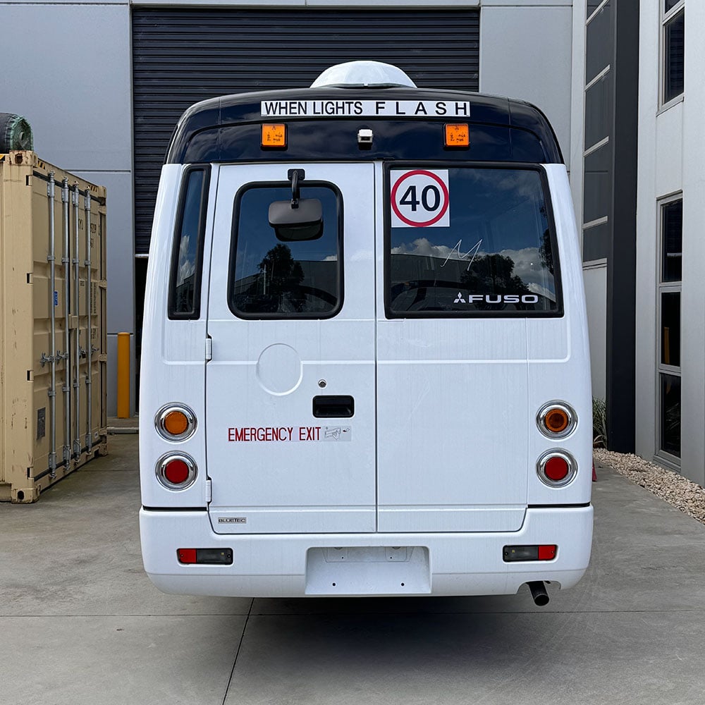 Photo of the rear of a Mitsubishi Rosa bus with NSW TS150 school bus lights and small 40km/h signage installed