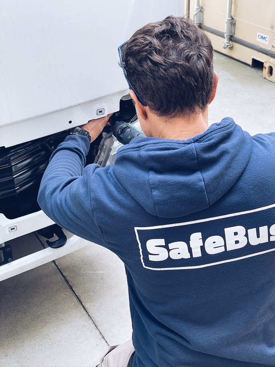 A Safebus employee working on the front of a Mitsubishi Rosa showing School Bus Safety Services