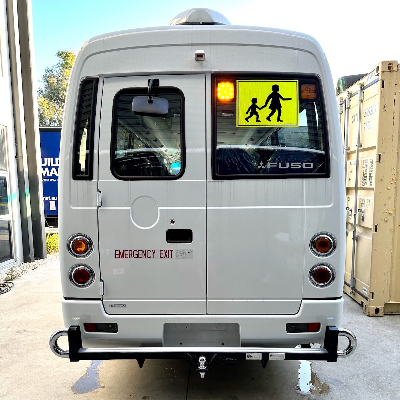 Photo of the rear of a 2024 5th generation BE7 Mitsubishi Rosa bus with Safebus SB001B window mount Victorian school bus lights and mother and child sign installed and tow bar with platform and chrome loop protectors