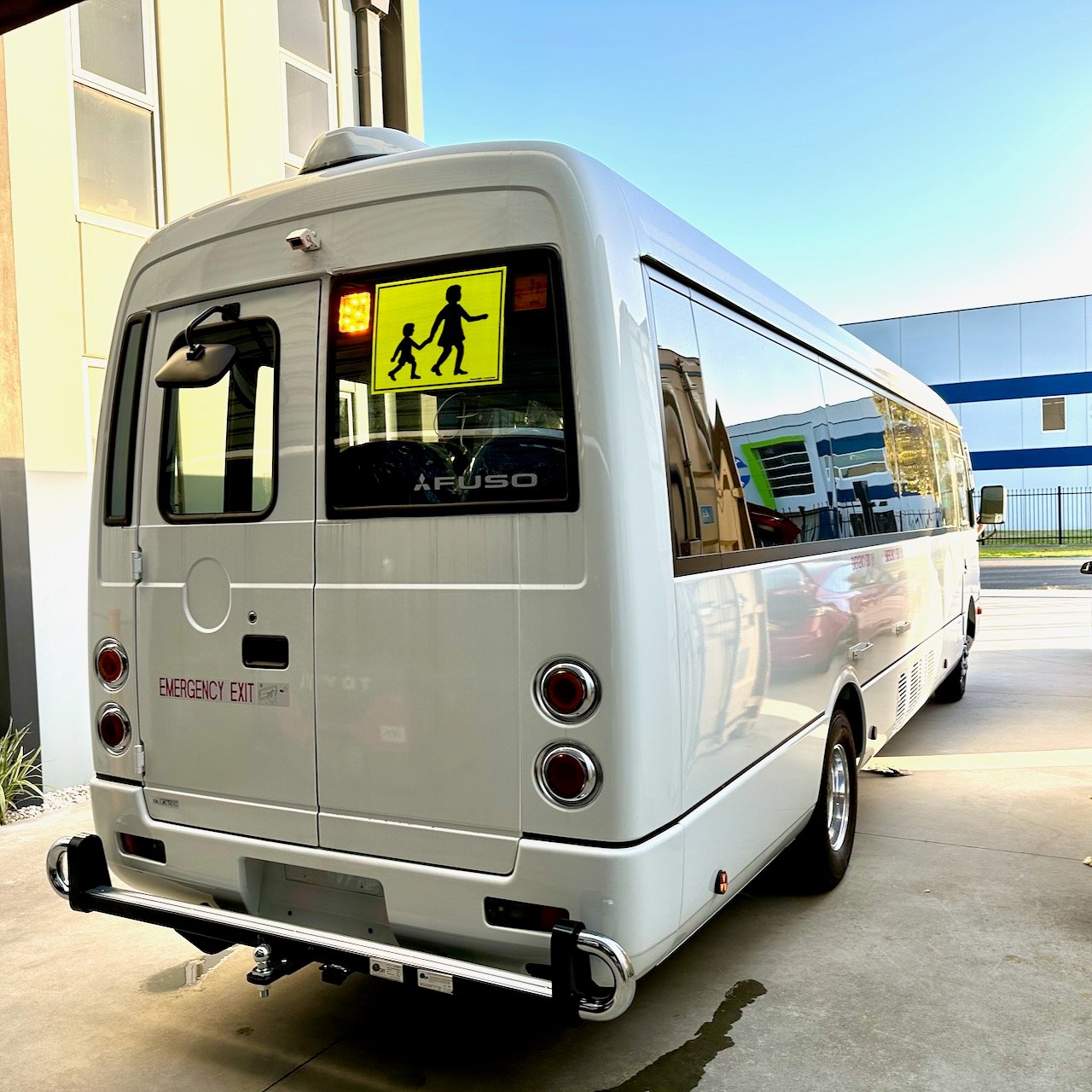 Photo of the rear of a 2024 5th generation BE7 Mitsubishi Rosa bus with Safebus SB001B window mount Victorian school bus lights and signage installed and tow bar with platform and chrome loop protectors